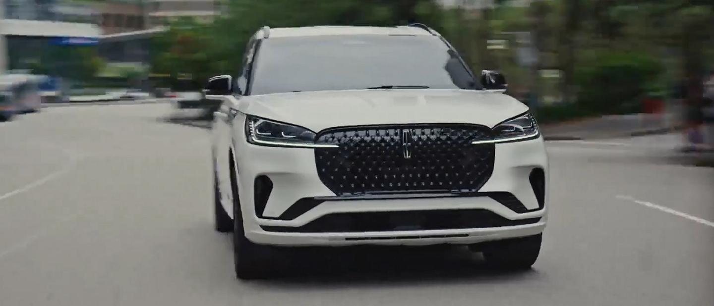 A 2026 Lincoln Aviator® SUV is being driven on a highway near a city