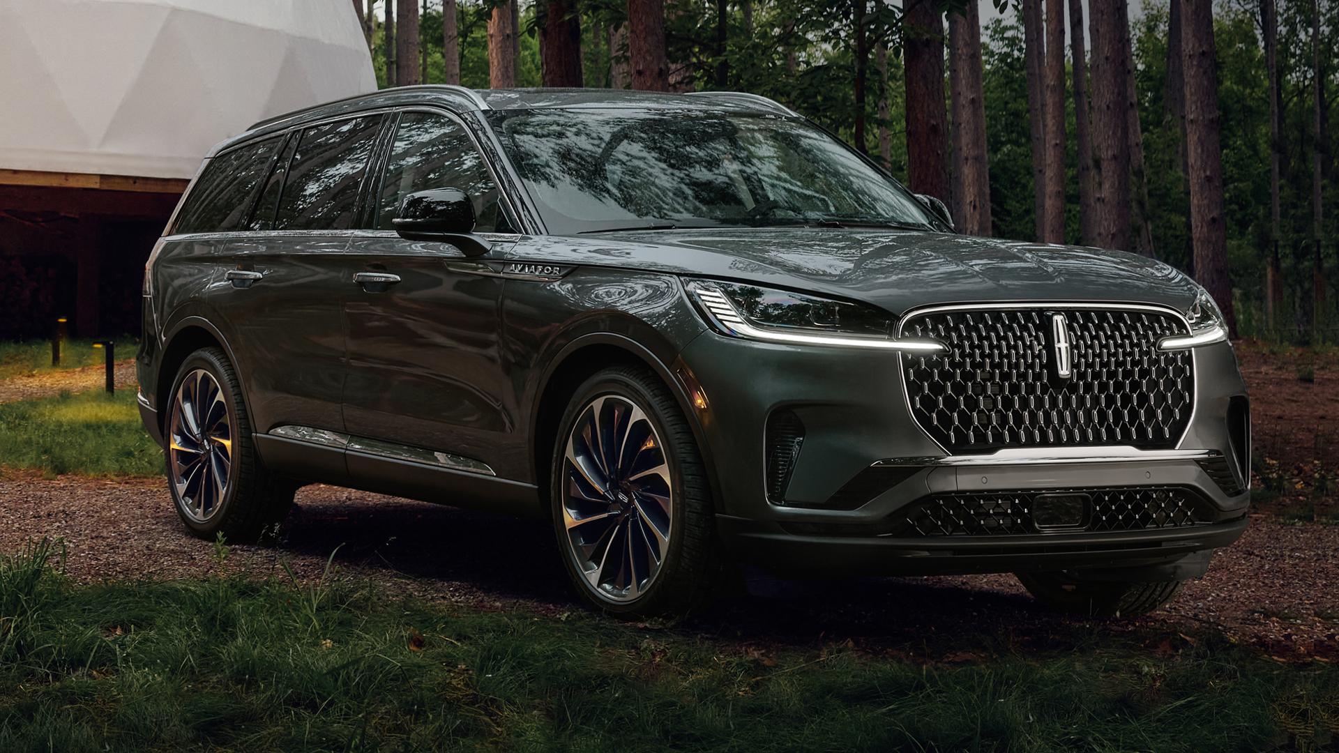 A 2027 Lincoln Aviator® SUV with its headlamps illuminated is being driven on a gravel road