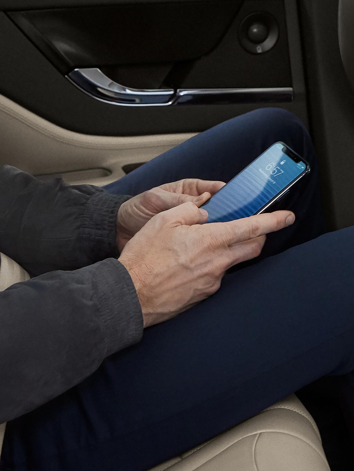 A man viewing  his cellphone while sitting inside a Lincoln vehicle.
