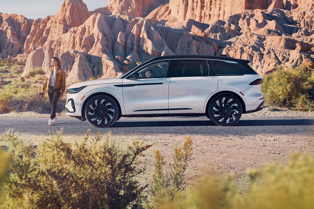 A Lincoln vehicle parked on a road with a woman walking next to it.