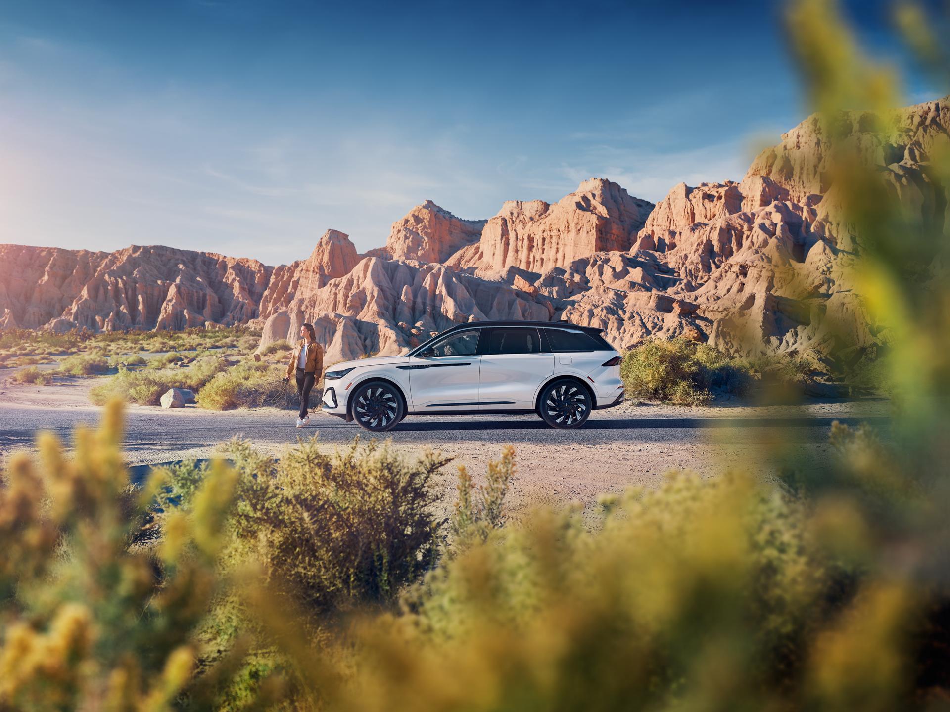A Lincoln vehicle parked on a road with a woman walking next to it.