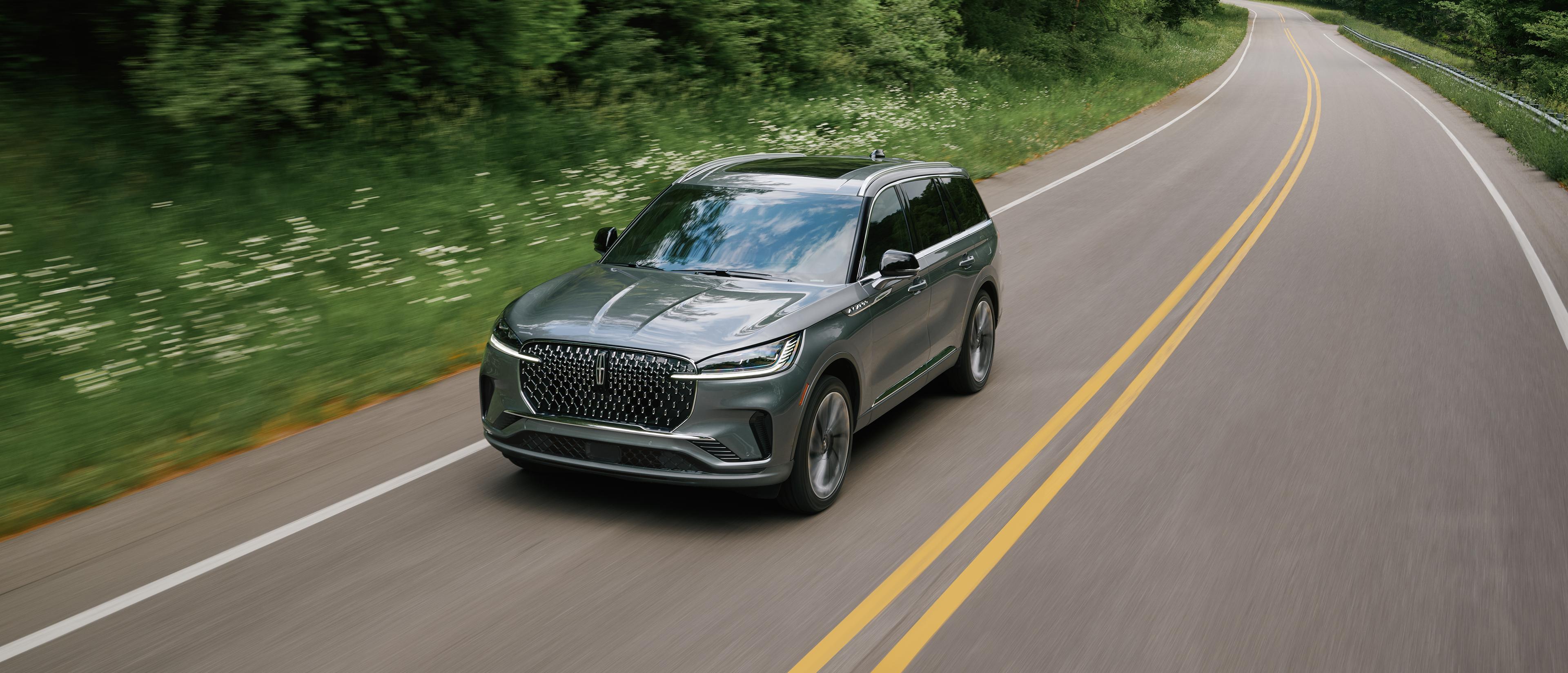 A 2027 Lincoln Aviator® SUV is being driven on a tree lined country road