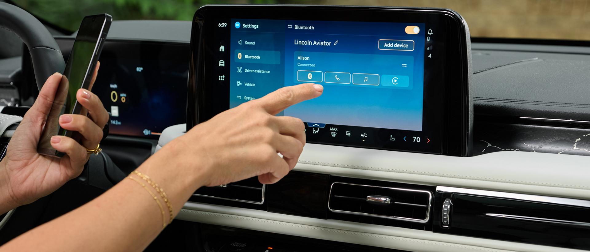 A hand reaches out to interact with the center touchscreen of a 2027 Lincoln Aviator® SUV