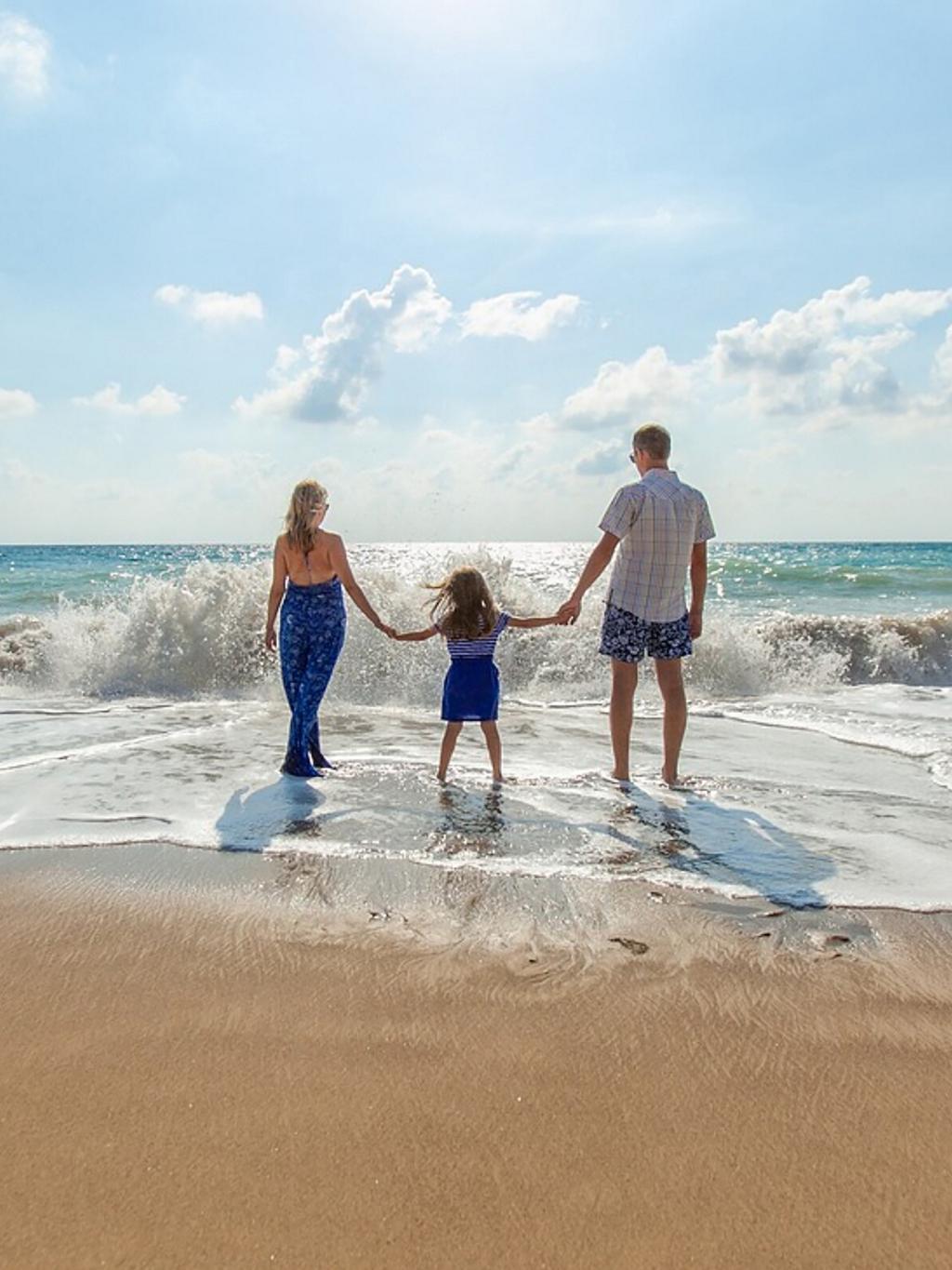 A family standing in the sand on the beach facing the water