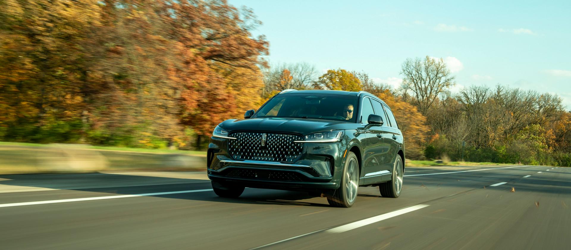 A 2026 Lincoln Aviator® SUV is shown driving on a tree-lined road