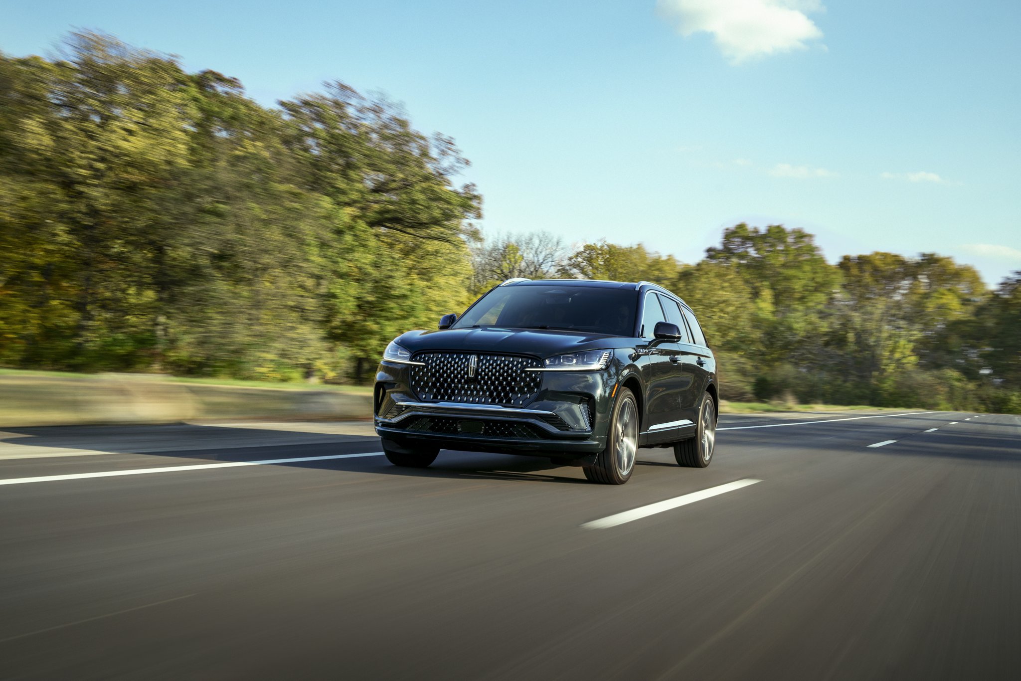 A 2025 Lincoln Aviator® SUV is shown driving on a tree-lined road.