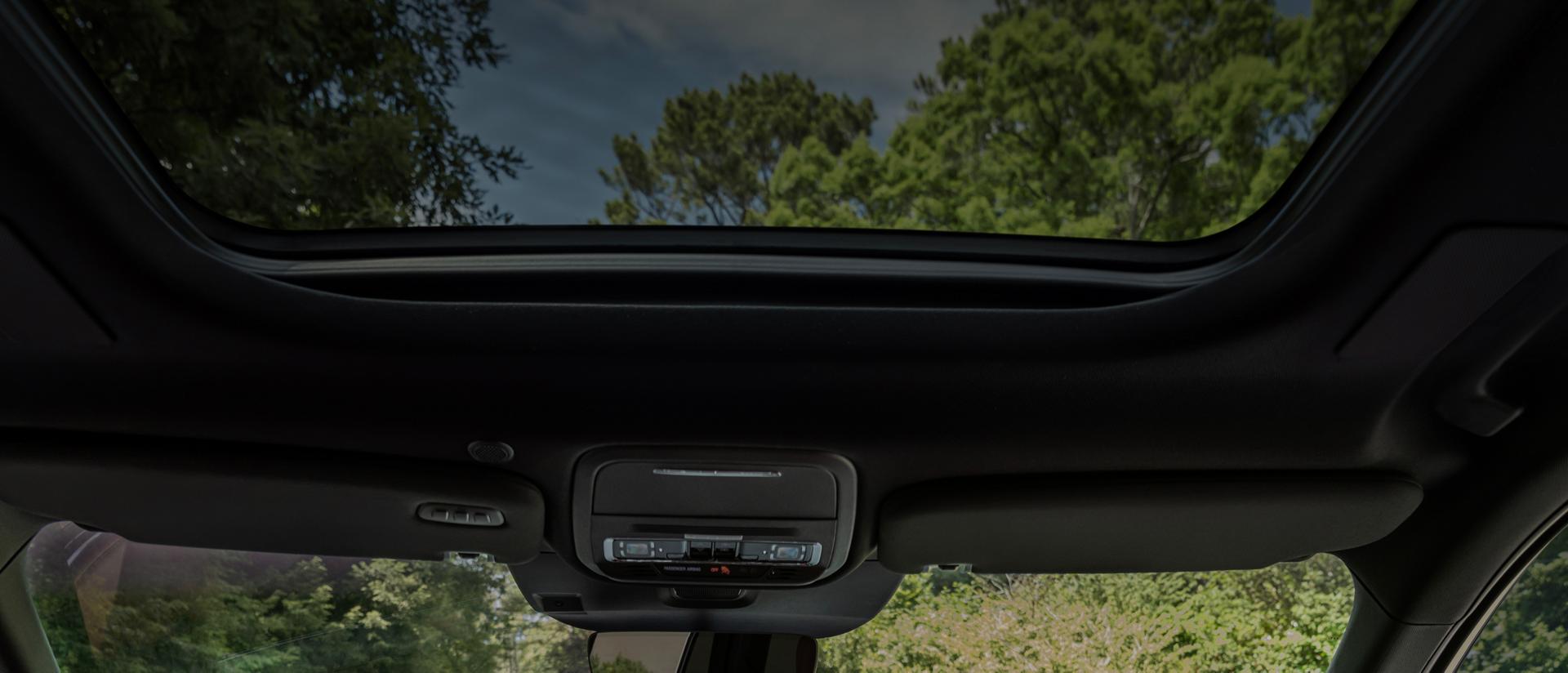A lush forest scene is shown through the front windshield and panoramic Vista Roof® of a 2027 Lincoln Aviator® SUV