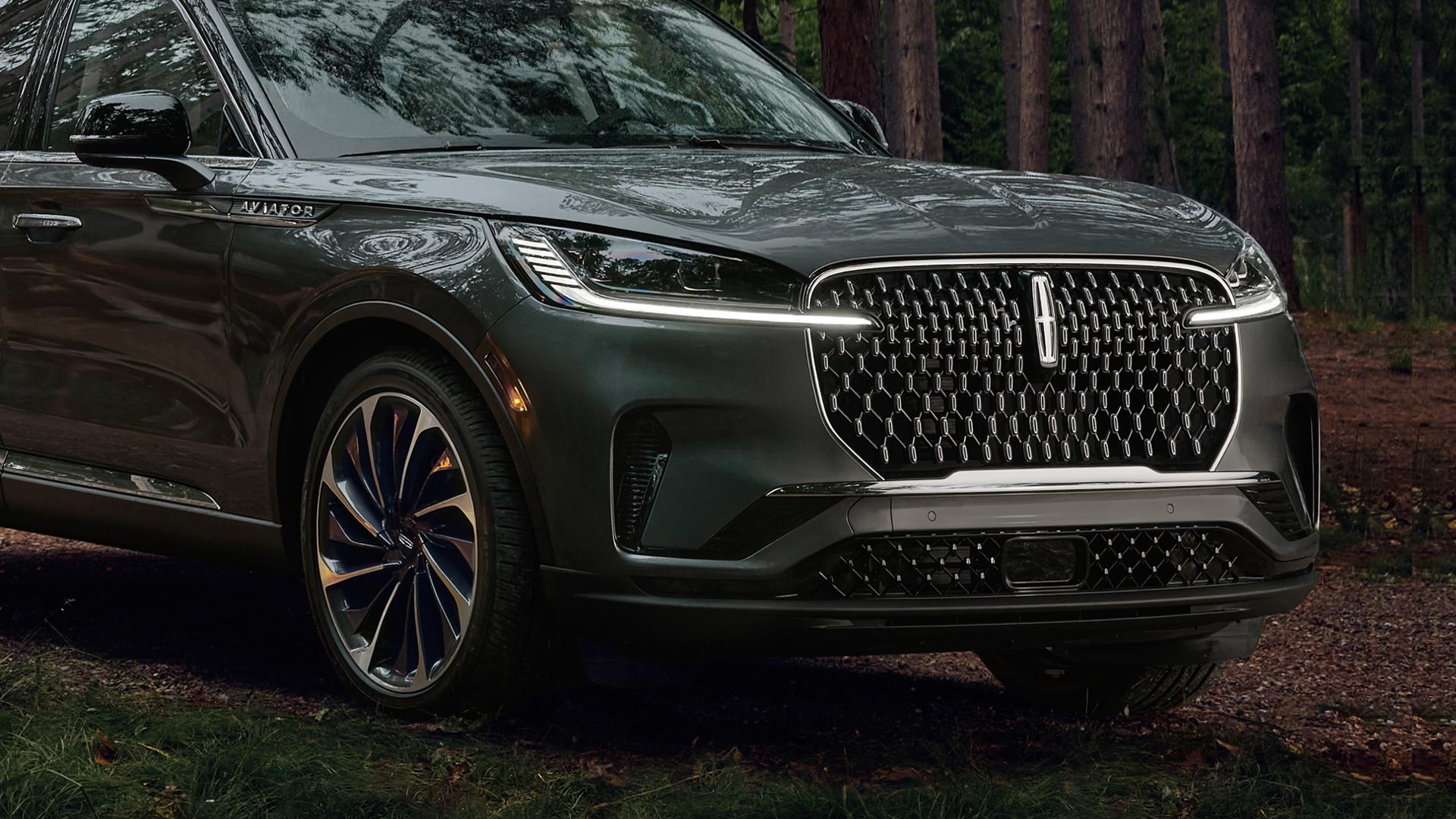 Una SUV Lincoln Aviator® 2027 con los faros delanteros iluminados circulando por una carretera de grava