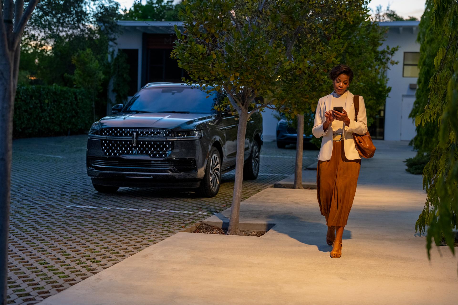 A woman accesses an app on her phone as she walks away from her parked 2027 Lincoln Navigator® SUV