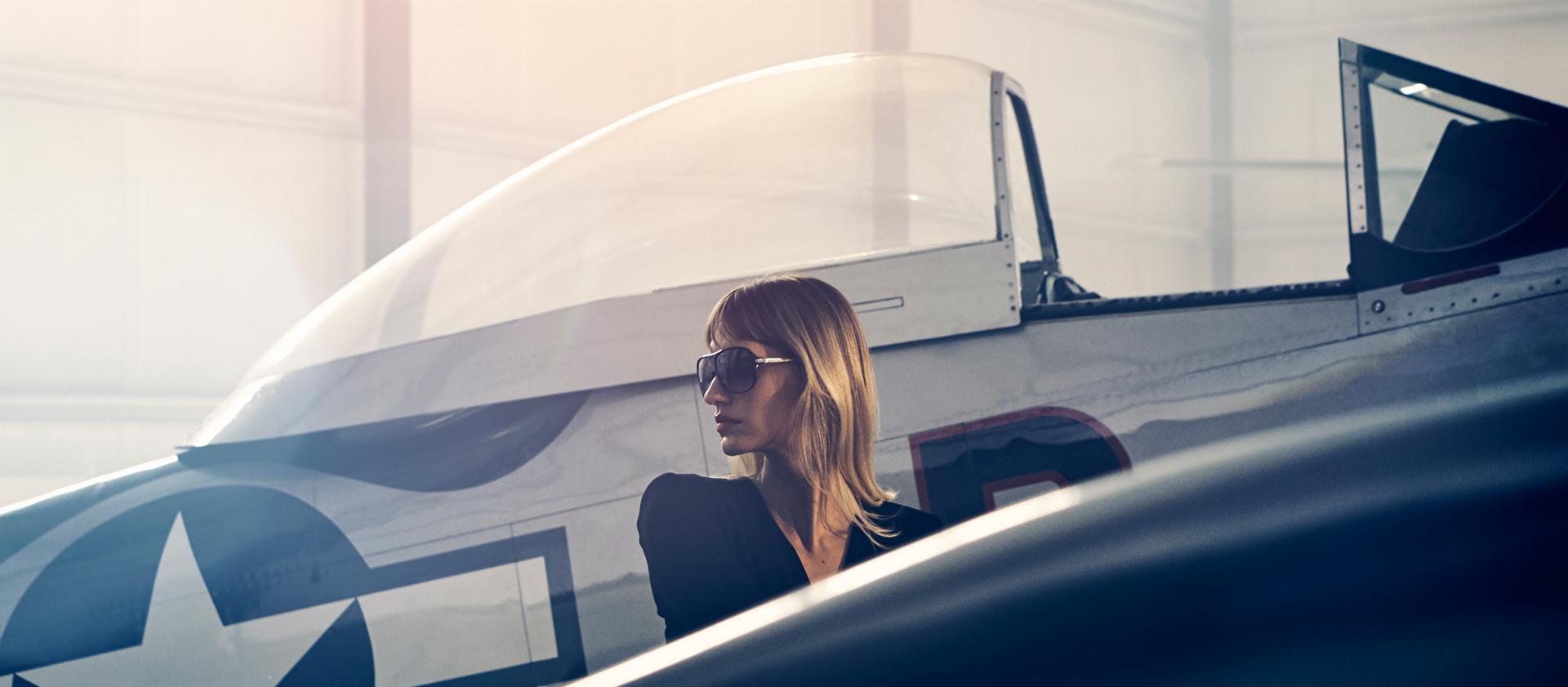 A woman walks past a vintage airplane in a private hangar