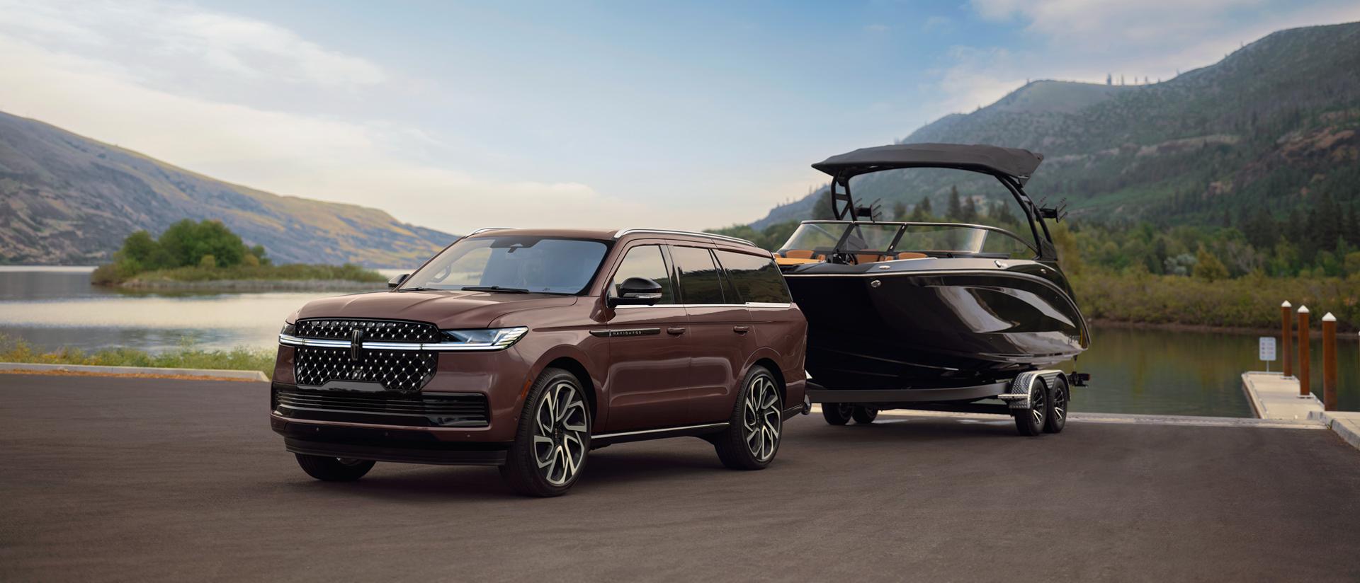 A 2027 Lincoln Navigator® SUV with a boat on a trailer is parked at a scenic boat ramp
