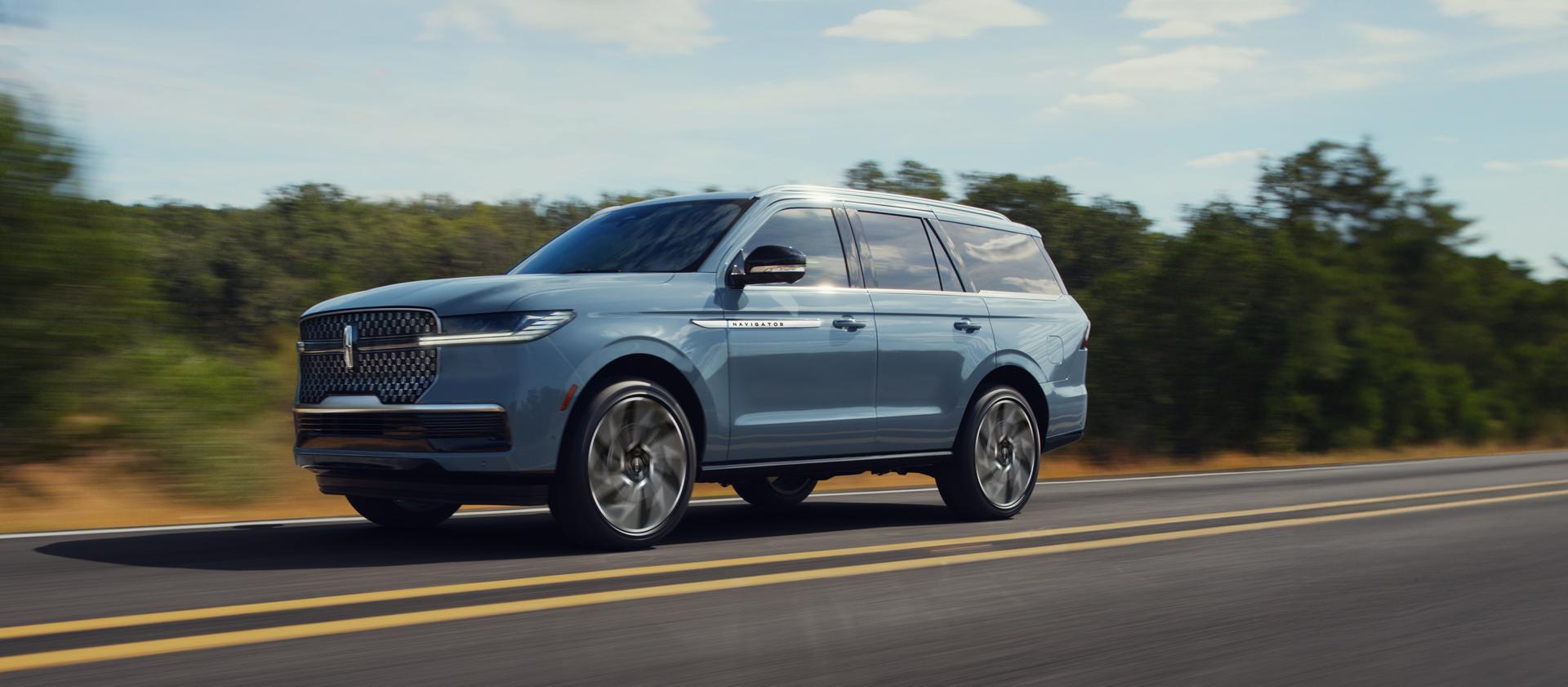 A 2026 Lincoln Navigator® Reserve in Gray Mist drives on a road with trees in the background