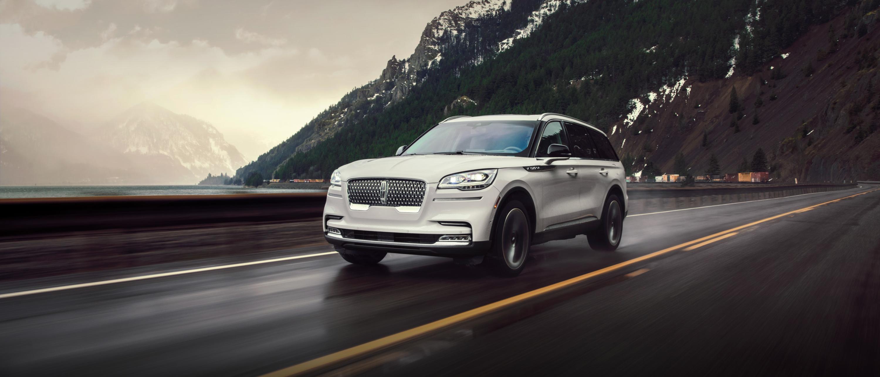 A Lincoln Aviator® SUV drives on a mountain road past a lake