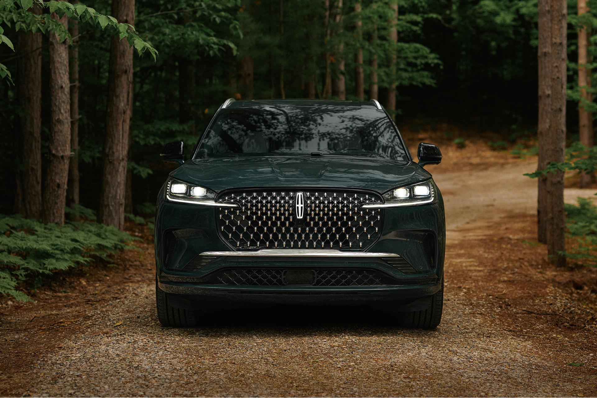 SUV Lincoln Aviator de lujo oscuro estacionado en un camino de tierra en un denso bosque verde.