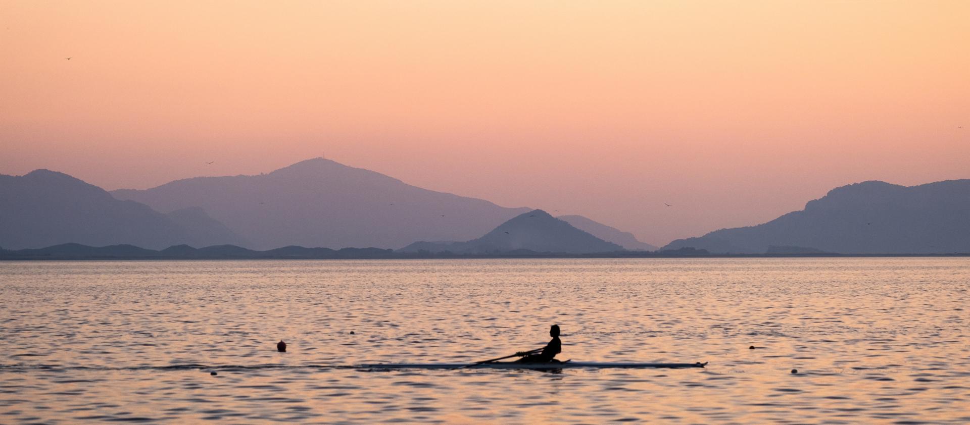A person rows a scull boat in the ocean in the morning