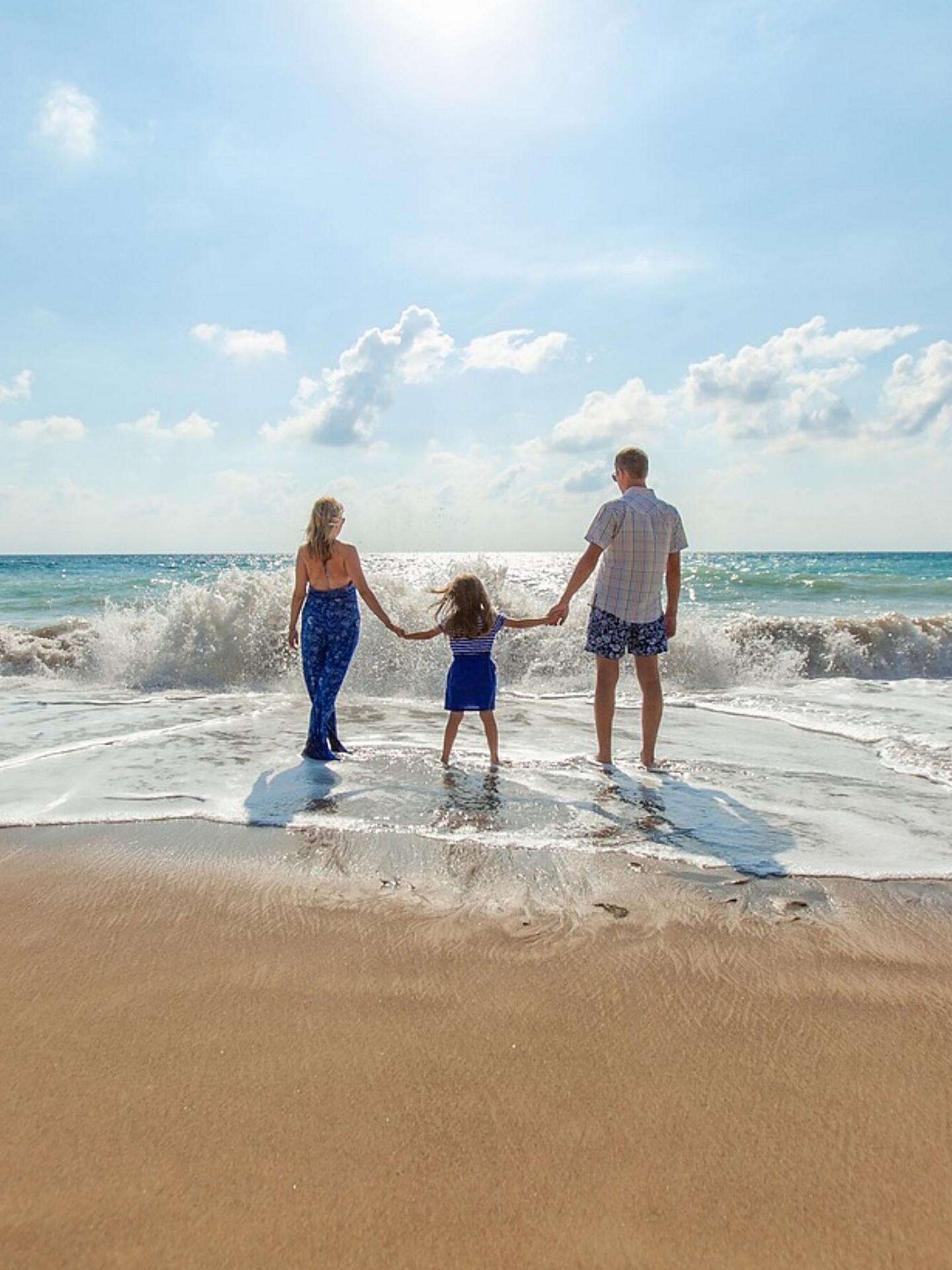 A family of three walk in the surf of an ocean