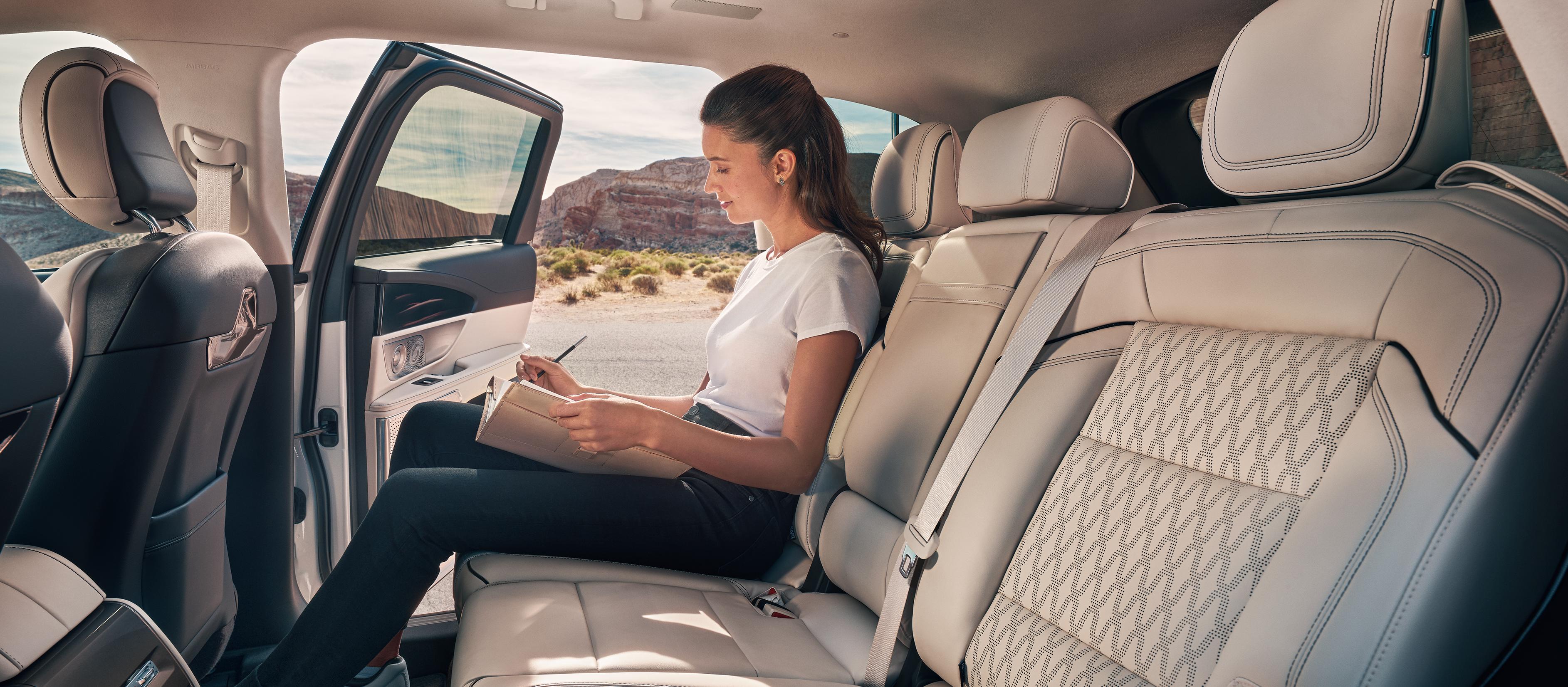 A woman journals in the second row of a Lincoln Black Label™ Nautilus® SUV