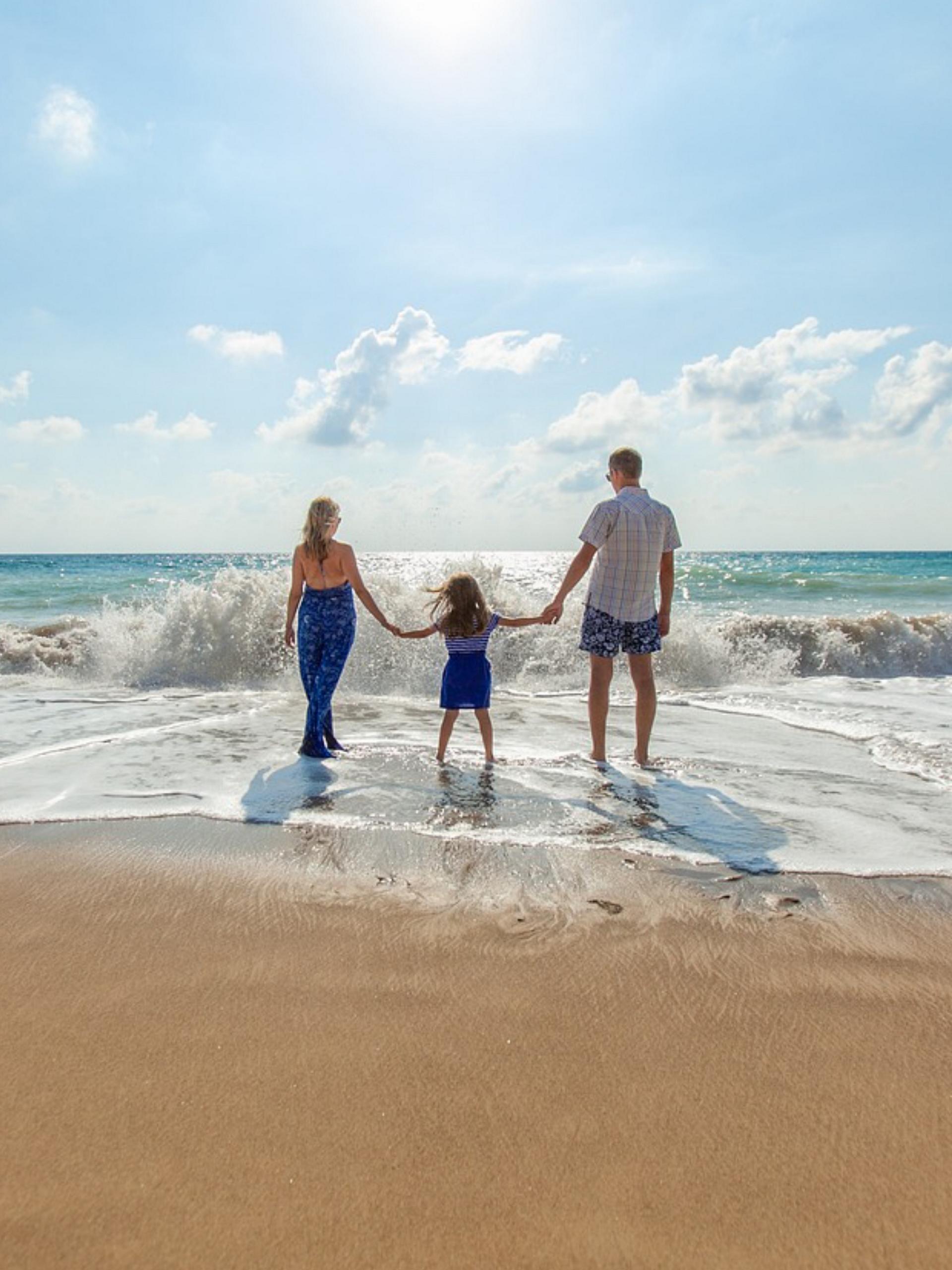 A family of three walk in the surf of an ocean
