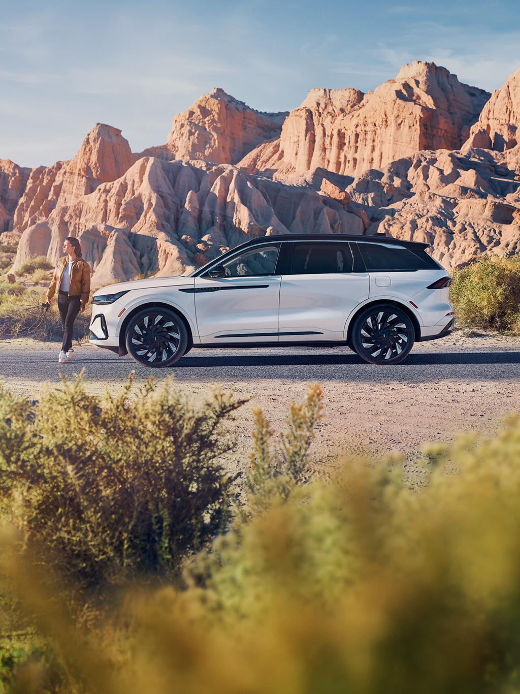 A woman standing outside her Lincoln vehicle with mountains in the background.