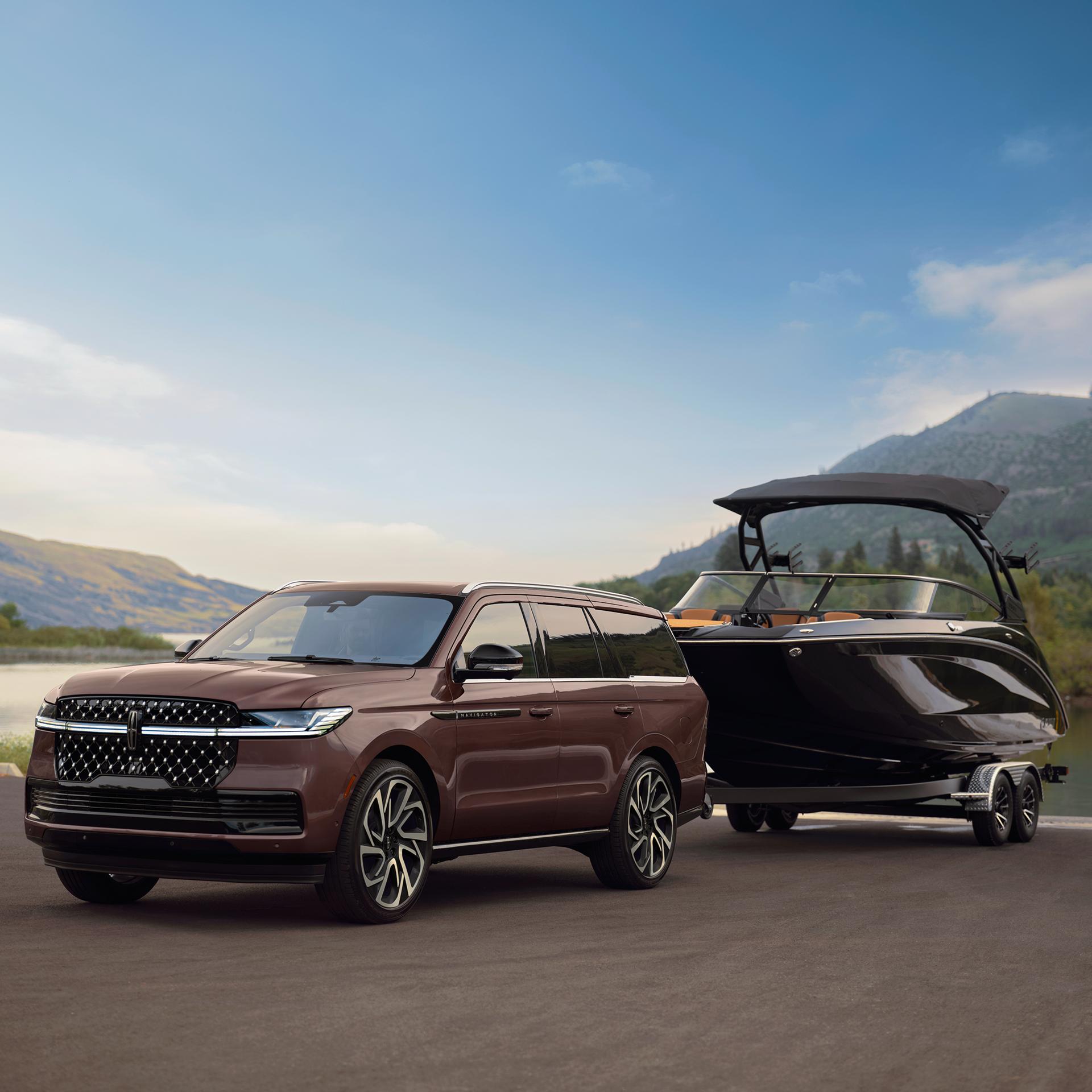A 2027 Lincoln Navigator® Black Label™ model is parked in front of a scenic waterfront with a pleasure boat hitched up