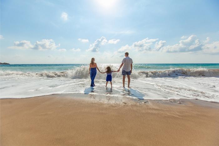 A family of three walk in the surf of an ocean