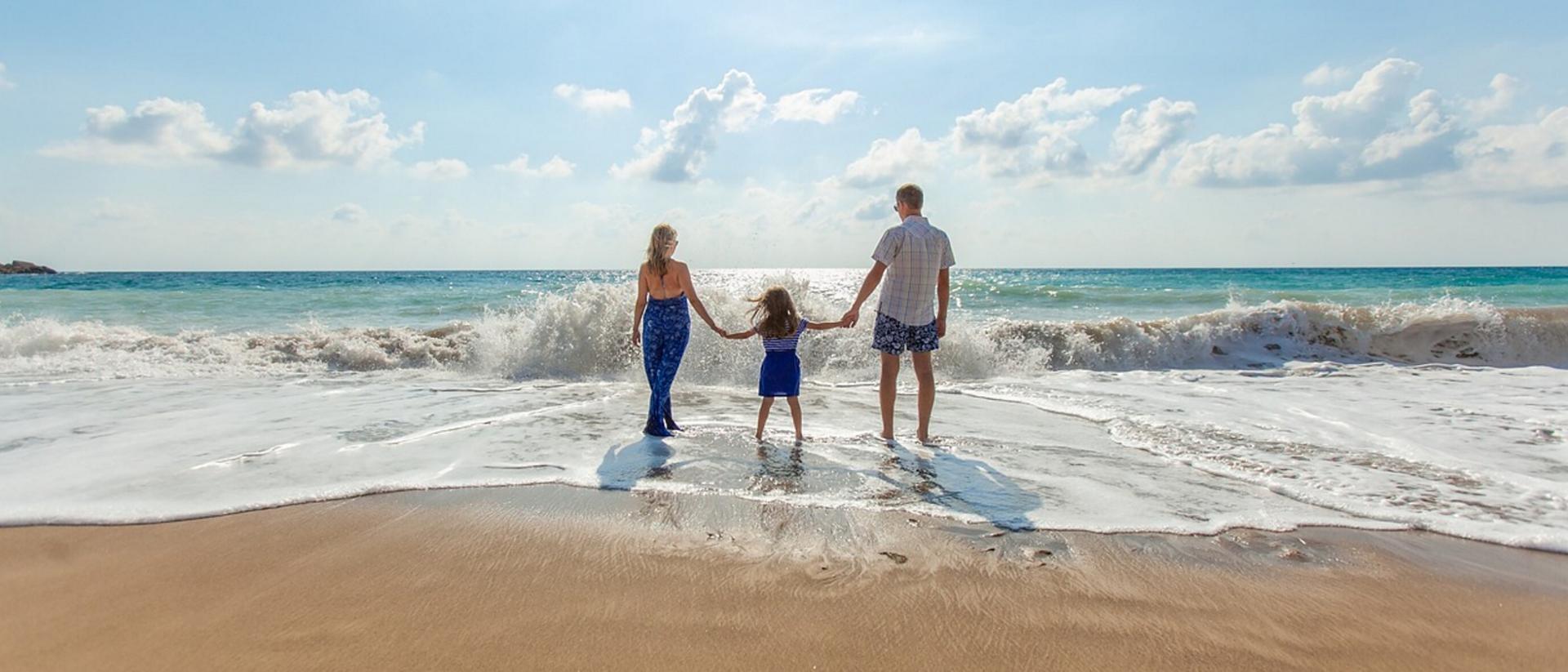 A family of three walk in the surf of an ocean