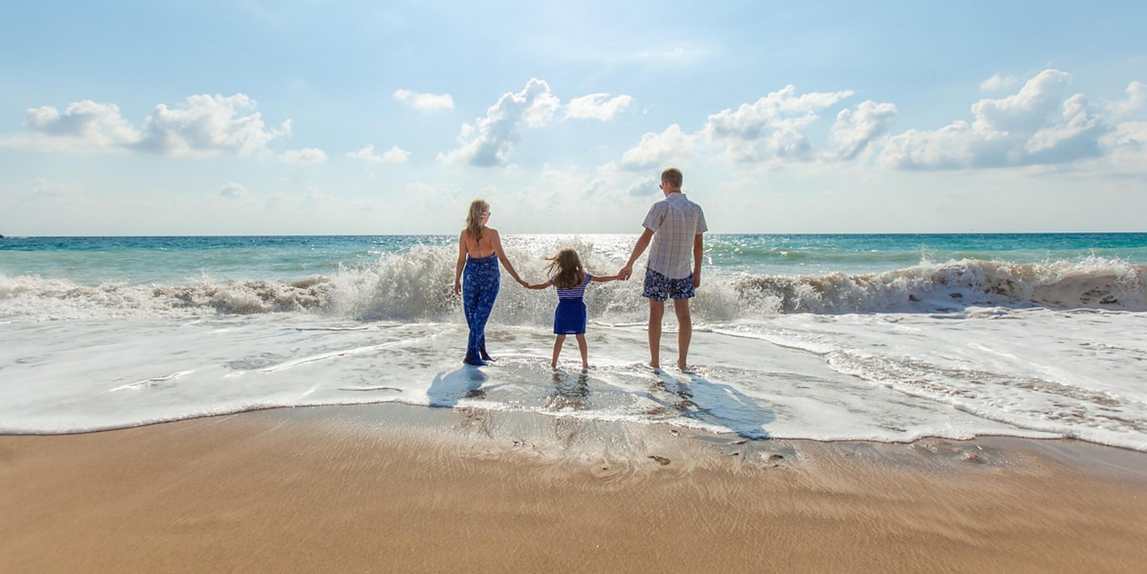 A family of three walk in the surf of an ocean