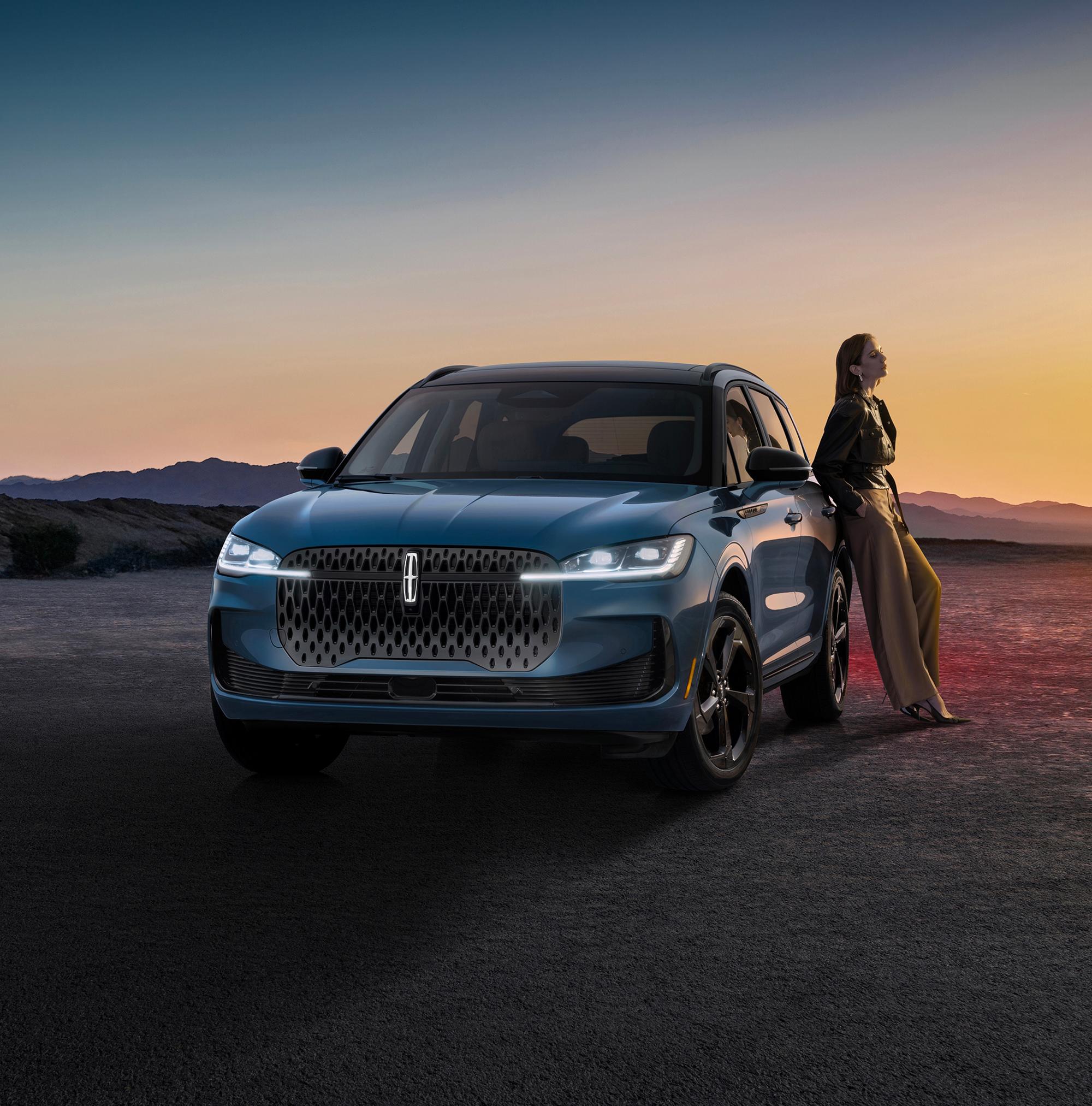A stylishly dressed woman leaning on a 2027 Lincoln Corsair® Hybrid parked in a dramatic desert landscape