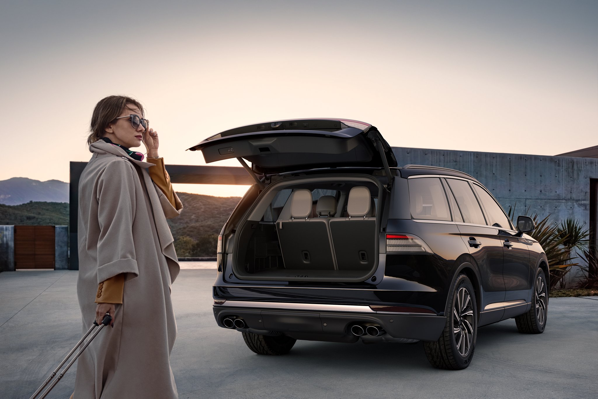 A woman standing behind her Lincoln vehicle with the trunk open.