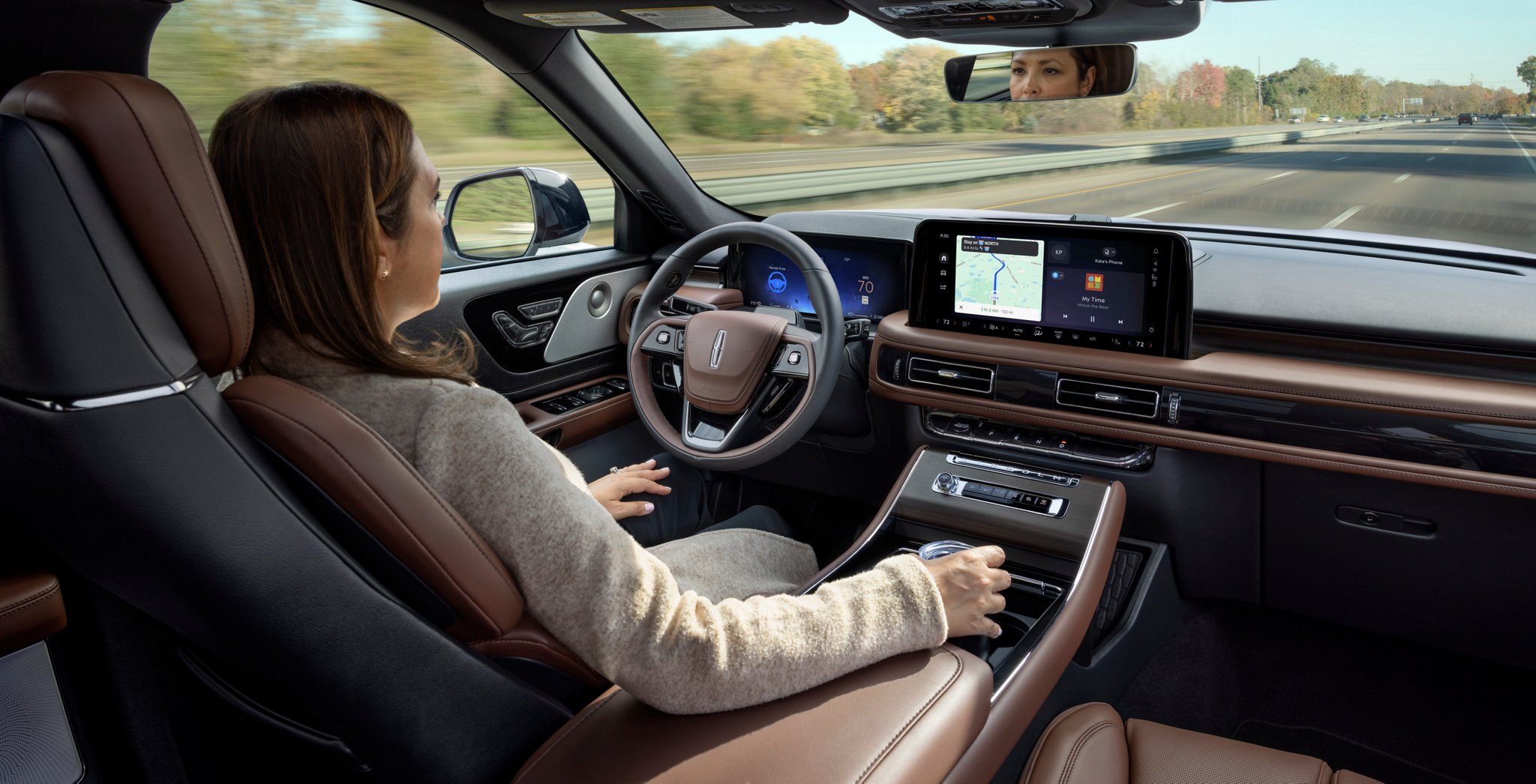 A 2025 Lincoln Aviator® SUV is being driven hands-free on a highway with Lincoln BlueCruise near a forest.